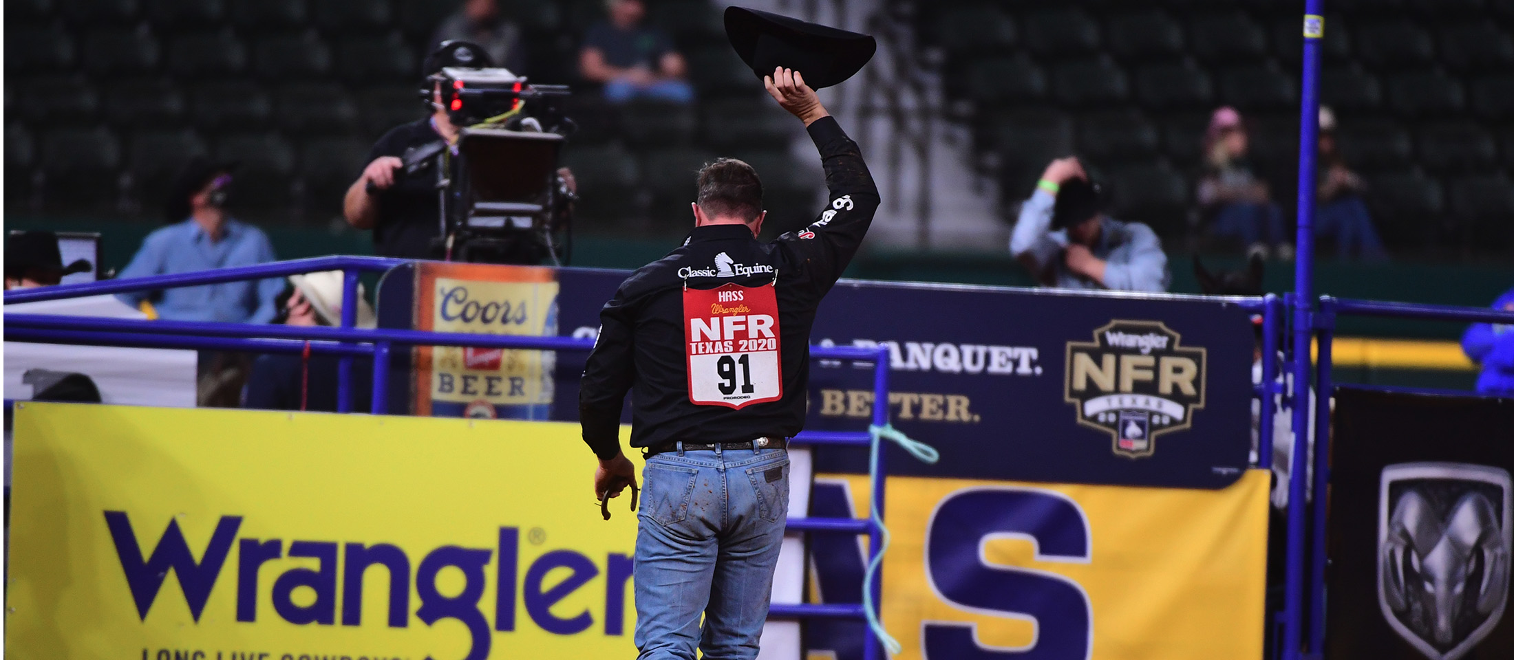 Cowboy walking away from camera with his right hand holding his cowboy hat in the air at the National Finals Rodeo.